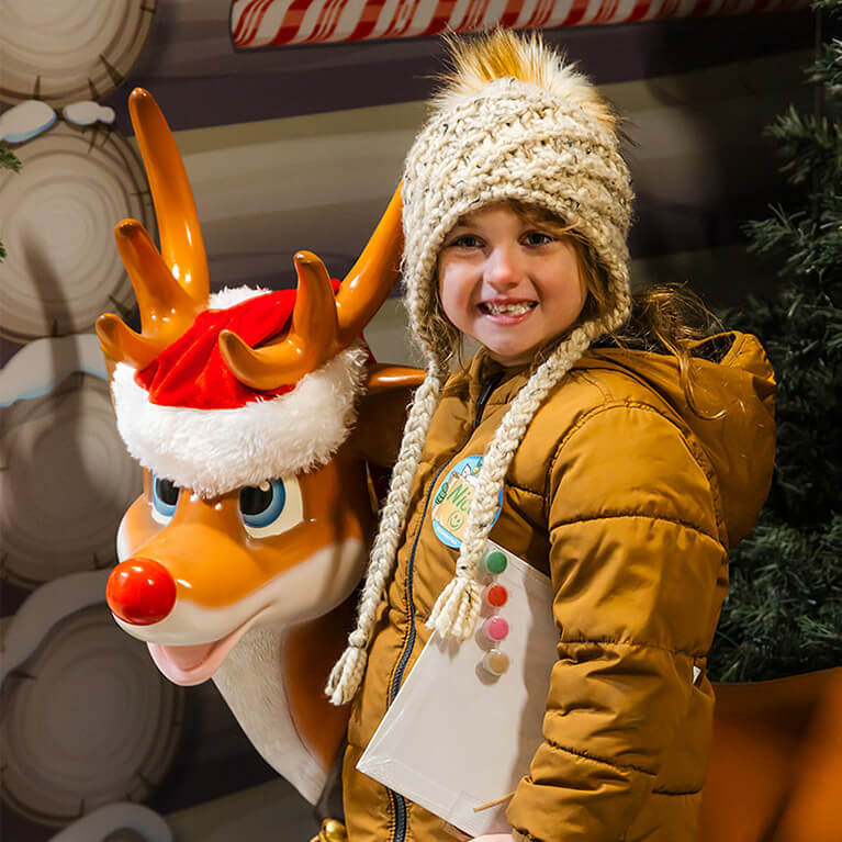 A young child posing with a Rudolph the red nosed reindeer figure.